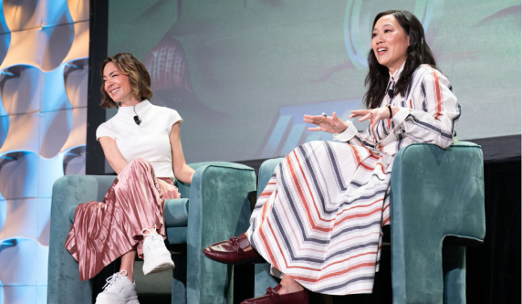 Priscilla Chan and Emily Chang sit on stage at SXSW for a panel discussion. Priscilla gestures while speaking, and Emily smiles. They sit in green chairs against a stage backdrop.